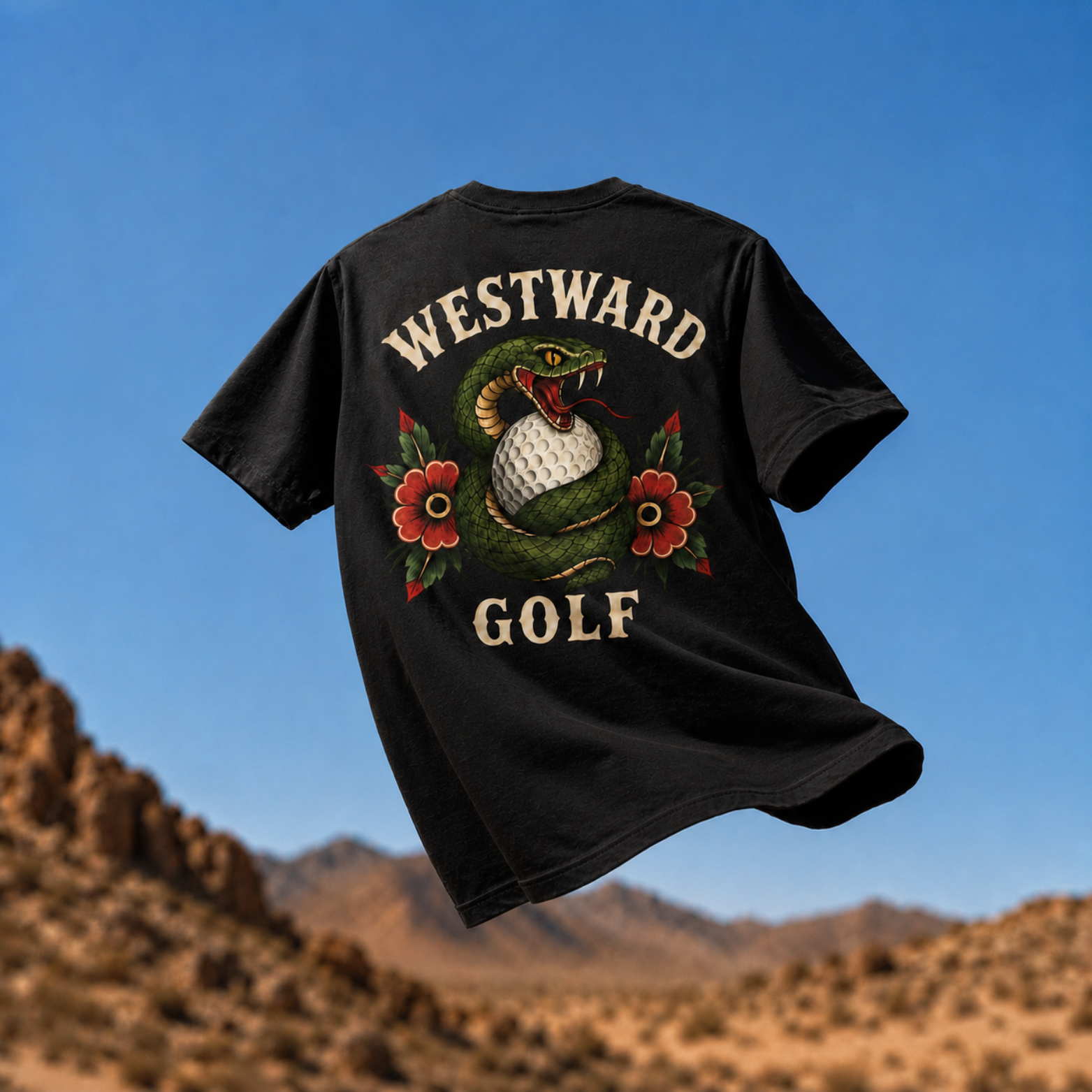Black Westward Golf snake graphic t-shirt floating over desert mountains with coiled snake golf ball design, red flowers, and bold cream back print