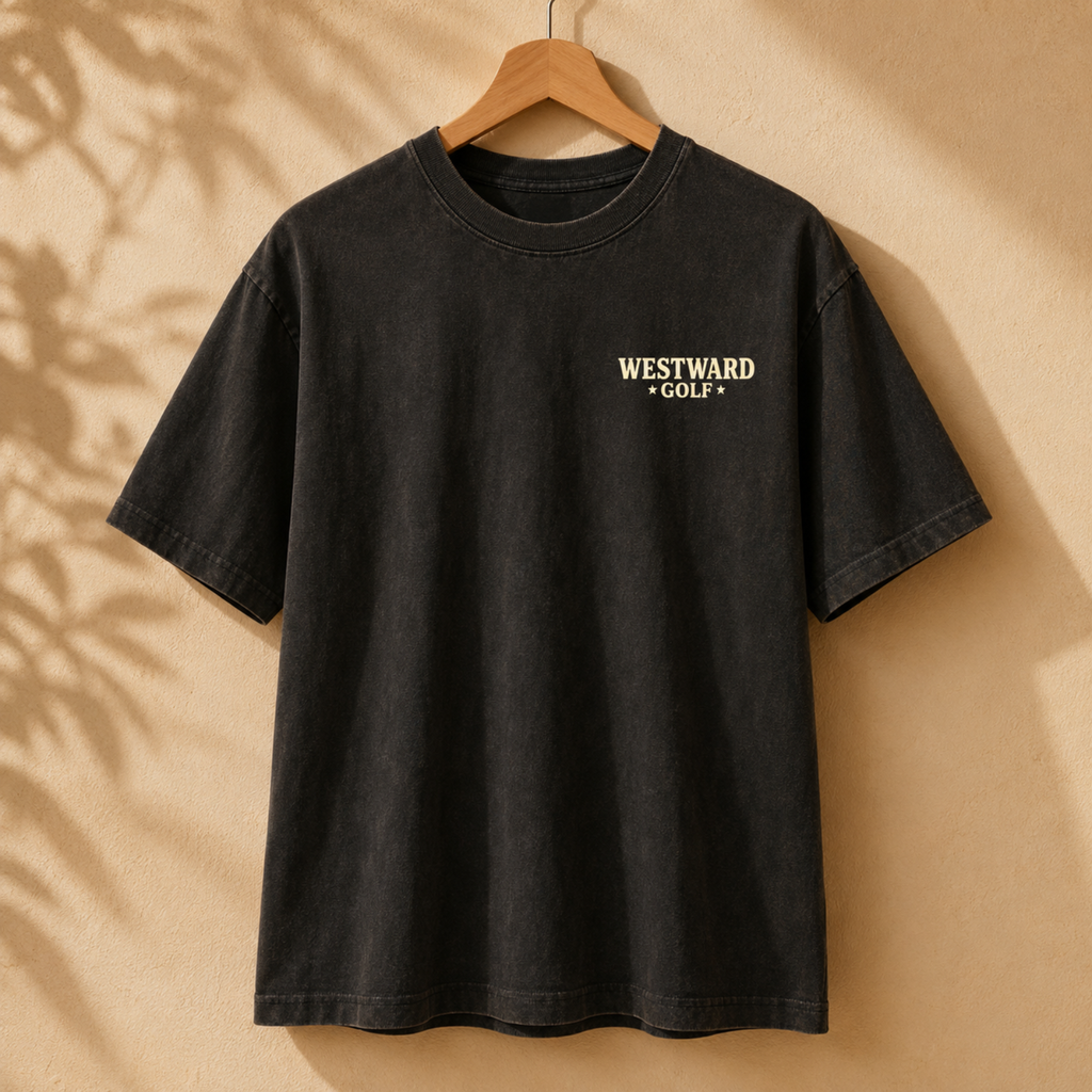 Black vintage-style Westward Golf t-shirt with small chest logo, heavyweight cotton look, oversized fit, and desert-inspired golf apparel aesthetic hanging on wooden hanger.