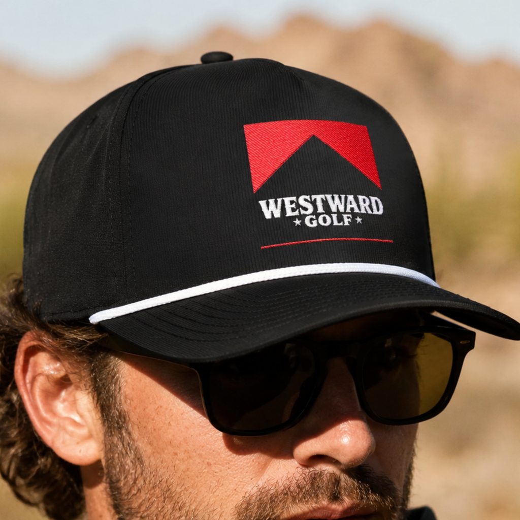 Close-up of black Westward Golf rope snapback hat worn outdoors with red embroidered western logo, white rope detail, structured crown, flat bill design, and premium men’s golf lifestyle headwear.