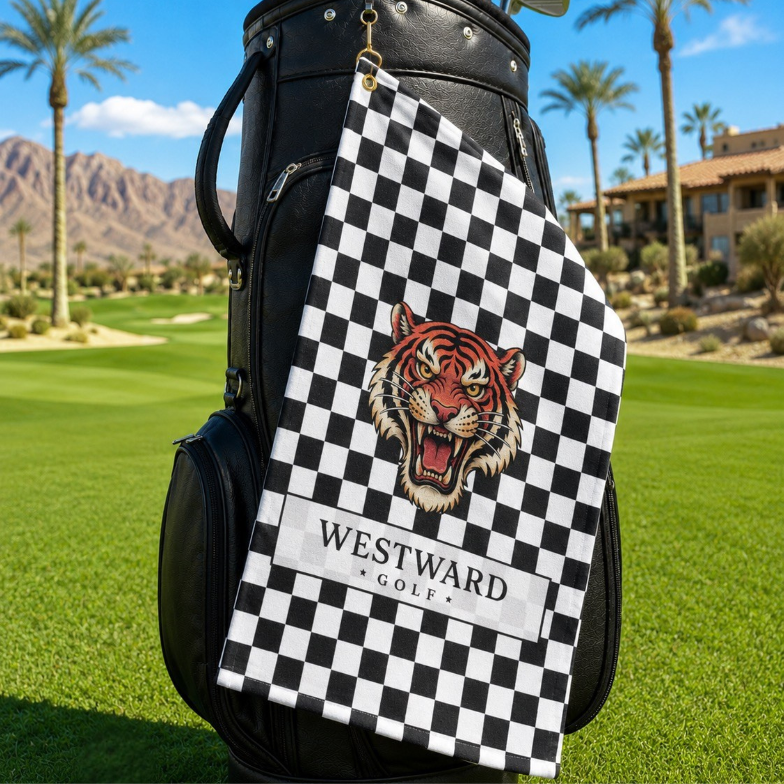 Black and white checkered Westward Golf towel hanging from a black golf bag, featuring a bold vintage roaring tiger logo, premium checkerboard golf towel with gold ring and brass grommet, stylish golf bag accessory for cleaning golf clubs, golf balls, grips, hands, and gear on the course.
