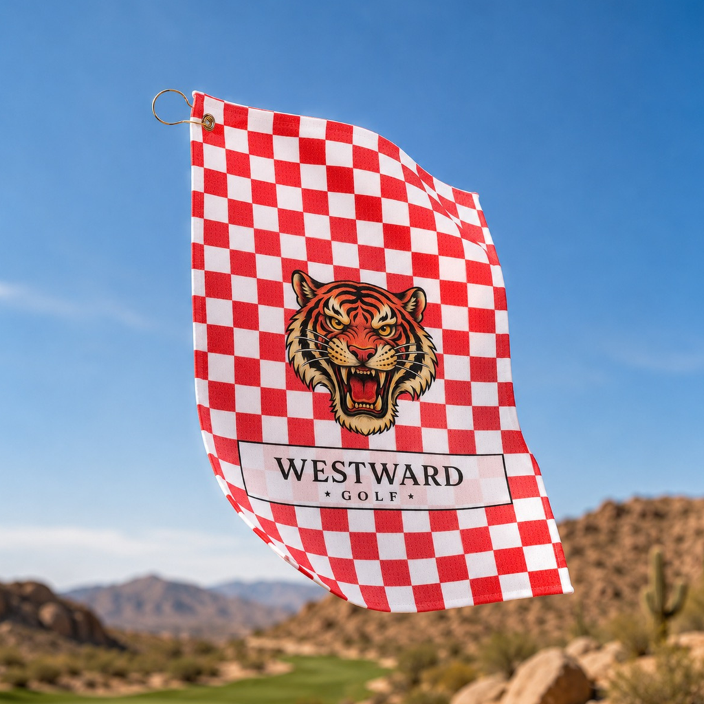 Red and white checkered Westward Golf towel flying outdoors with vintage roaring tiger logo, premium checkerboard golf towel with gold ring and brass grommet, bold golf bag accessory for cleaning golf clubs, golf balls, grips, hands, and gear on the course with desert mountain golf landscape background.