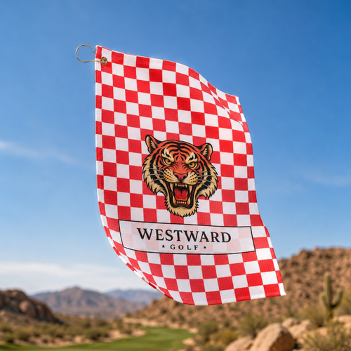 Red and white checkered Westward Golf towel flying outdoors with vintage roaring tiger logo, premium checkerboard golf towel with gold ring and brass grommet, bold golf bag accessory for cleaning golf clubs, golf balls, grips, hands, and gear on the course with desert mountain golf landscape background.