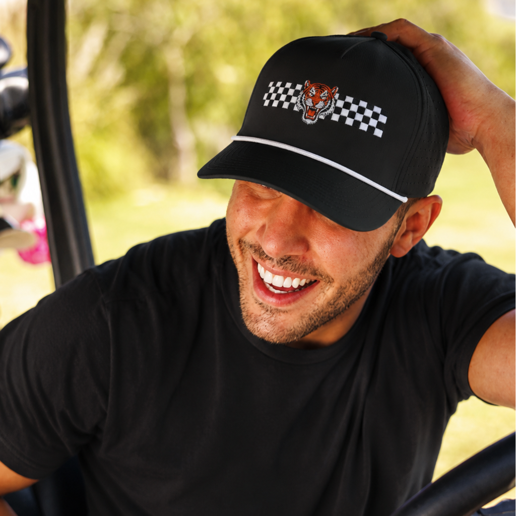 Golfer wearing a black cap with a tiger logo and checkered pattern, sitting in a golf cart.
