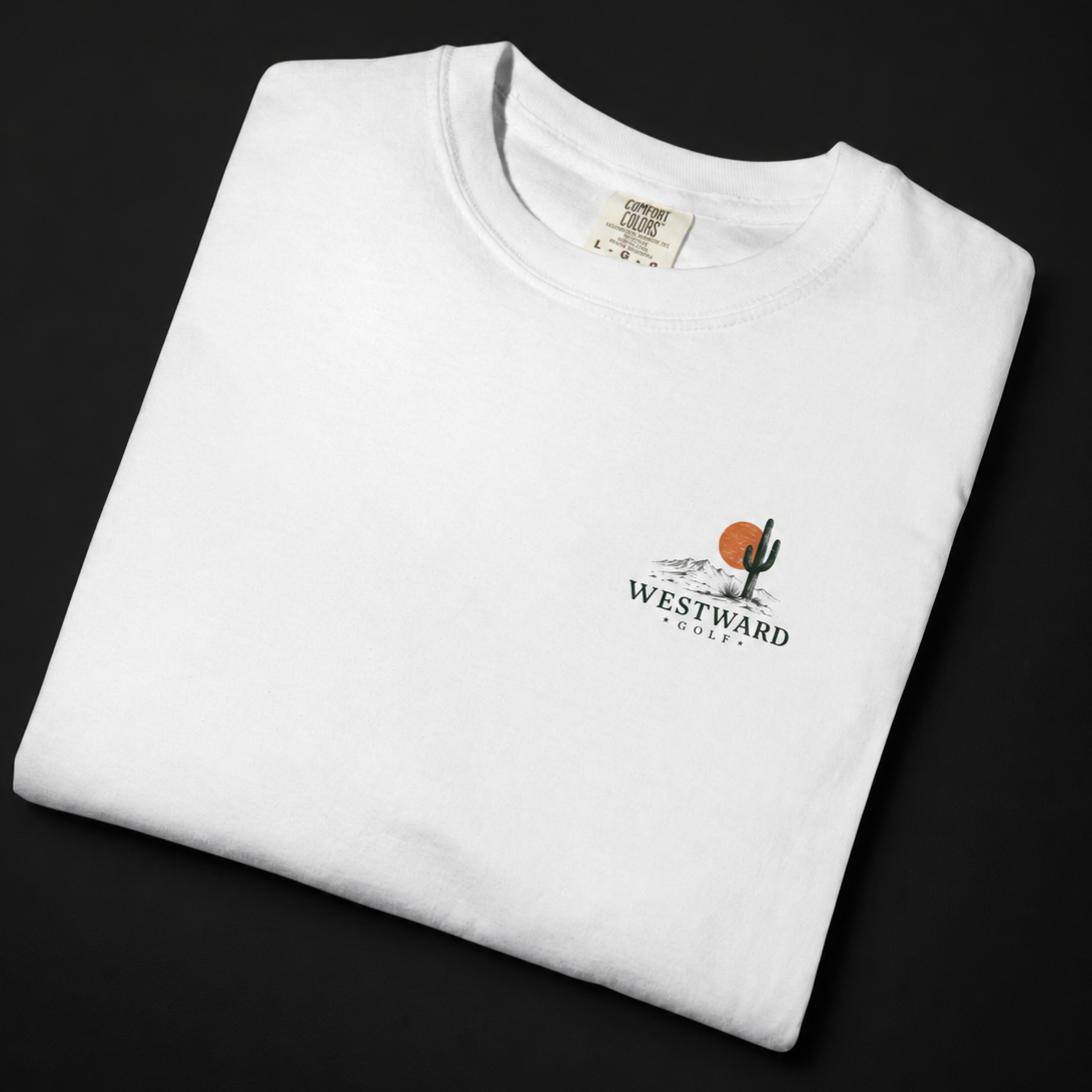 Folded white Westward Golf T-shirt mockup on black studio background, featuring small front chest desert golf logo with cactus, orange sunset, mountains, and Westward Golf branding.